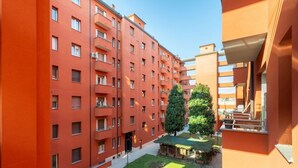 Un edificio residencial de varios pisos con balcones, un patio con césped y árboles, y un pequeño espacio de estar al aire libre.