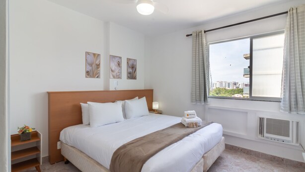 Una habitación de hotel con una cama grande, una mesita de noche, una ventana con cortinas y una obra de arte en la pared.