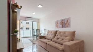 Un salón con un sofá color beige, una mesa de centro de cristal y una obra de arte colgada en la pared.