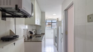 Una cocina estrecha con armarios blancos, un microondas y un tostador.