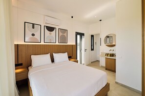Una moderna camera d'albergo con un letto grande, una testiera in legno, comodini, un armadio a muro, un bagno con lavandino e specchio, e opere d'arte astratte alle pareti.
