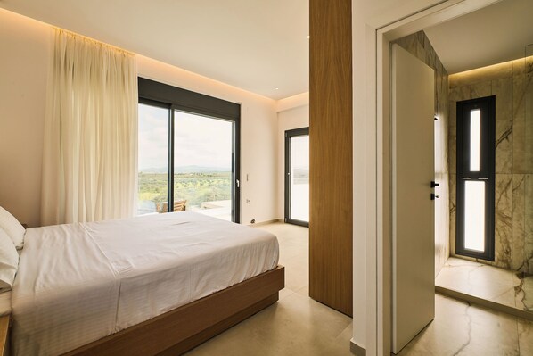 A bedroom with a large bed, a sliding glass door to a balcony, and a view of the outdoors. - POLYTELIA | Luxury Living (Hersonissos)