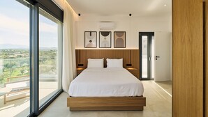 A modern bedroom with a large bed, a view of the outdoors, and a door leading to another room. - POLYTELIA | Luxury Living (Hersonissos)