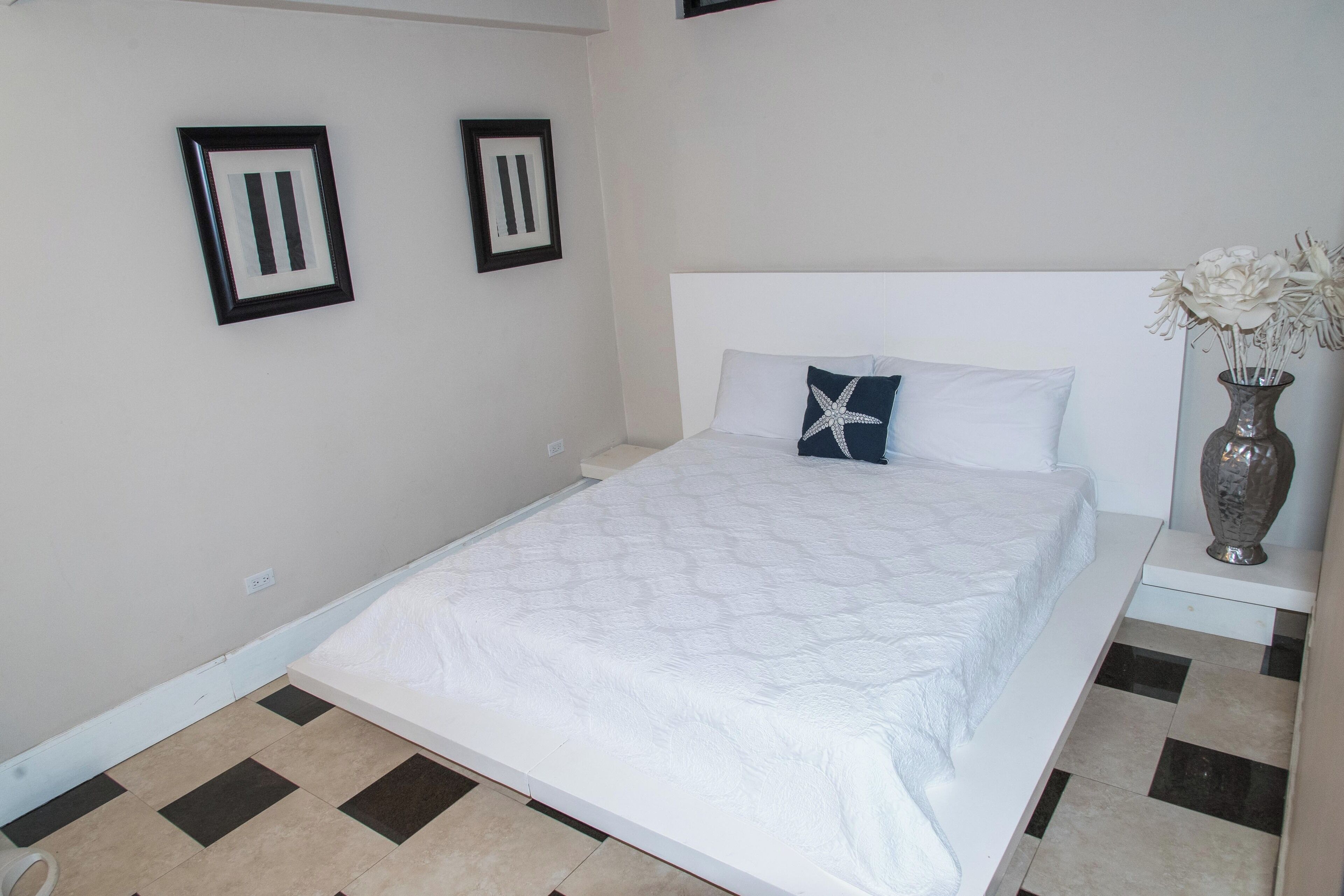 A neatly made bed with a white quilt, a starfish pillow, and a vase with flowers on a bedside table.