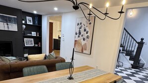 Un comedor con una mesa de madera, dos sillas grises, una araña y una escalera al fondo.