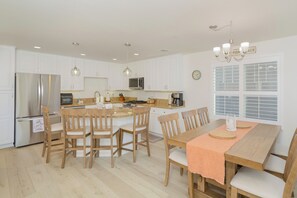 Een moderne keuken met witte kasten, roestvrijstalen apparatuur, houten stoelen en een eettafel met een perzikkleurige tafelrunner.