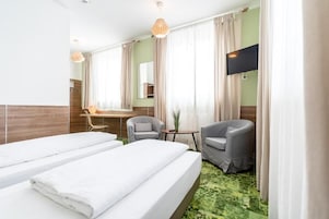 Quarto de hotel com duas camas, uma escrivaninha, duas cadeiras, uma televisão e um espelho.