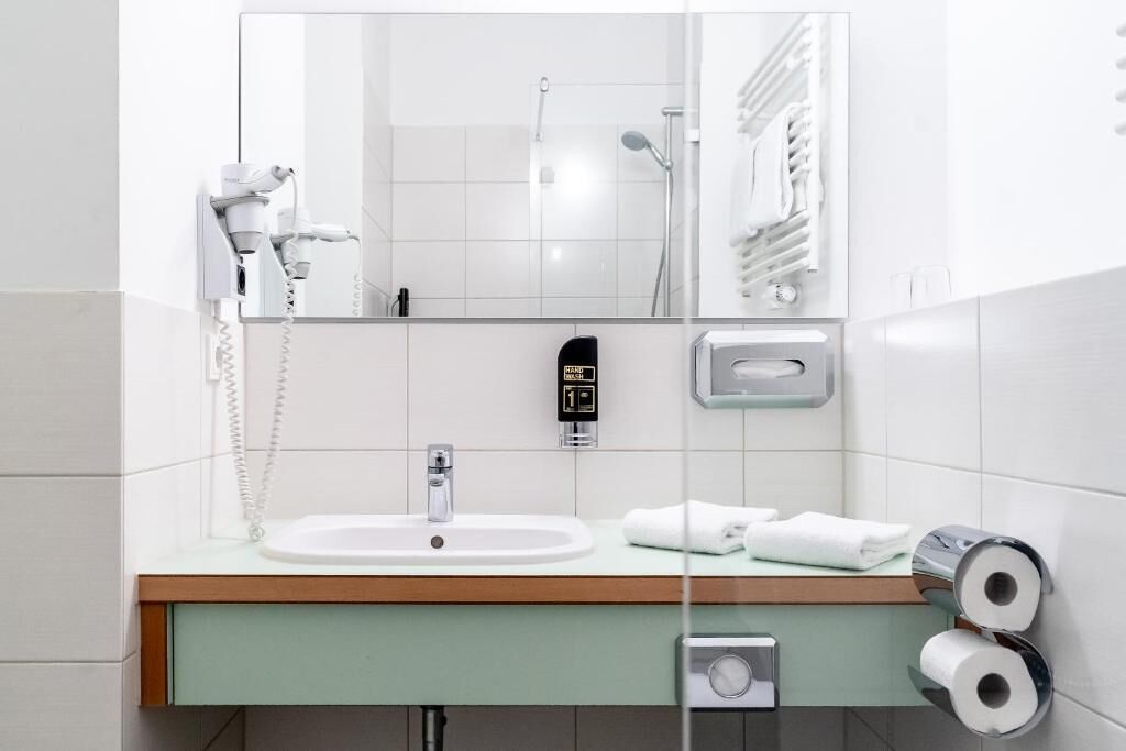 Un baño con lavamanos, espejo, secador de manos y barra para toallas.