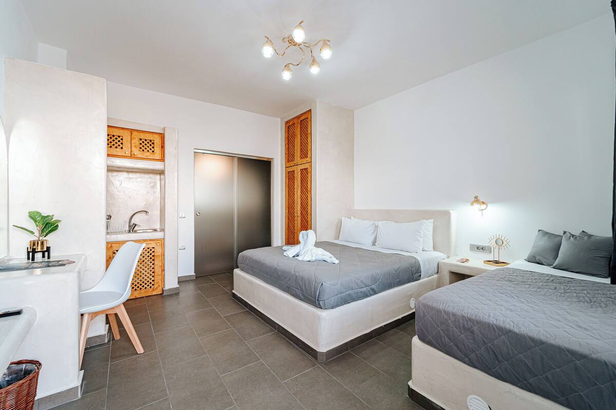 Et moderne hotelværelse med to senge, et skrivebord og et lille tekøkken.
