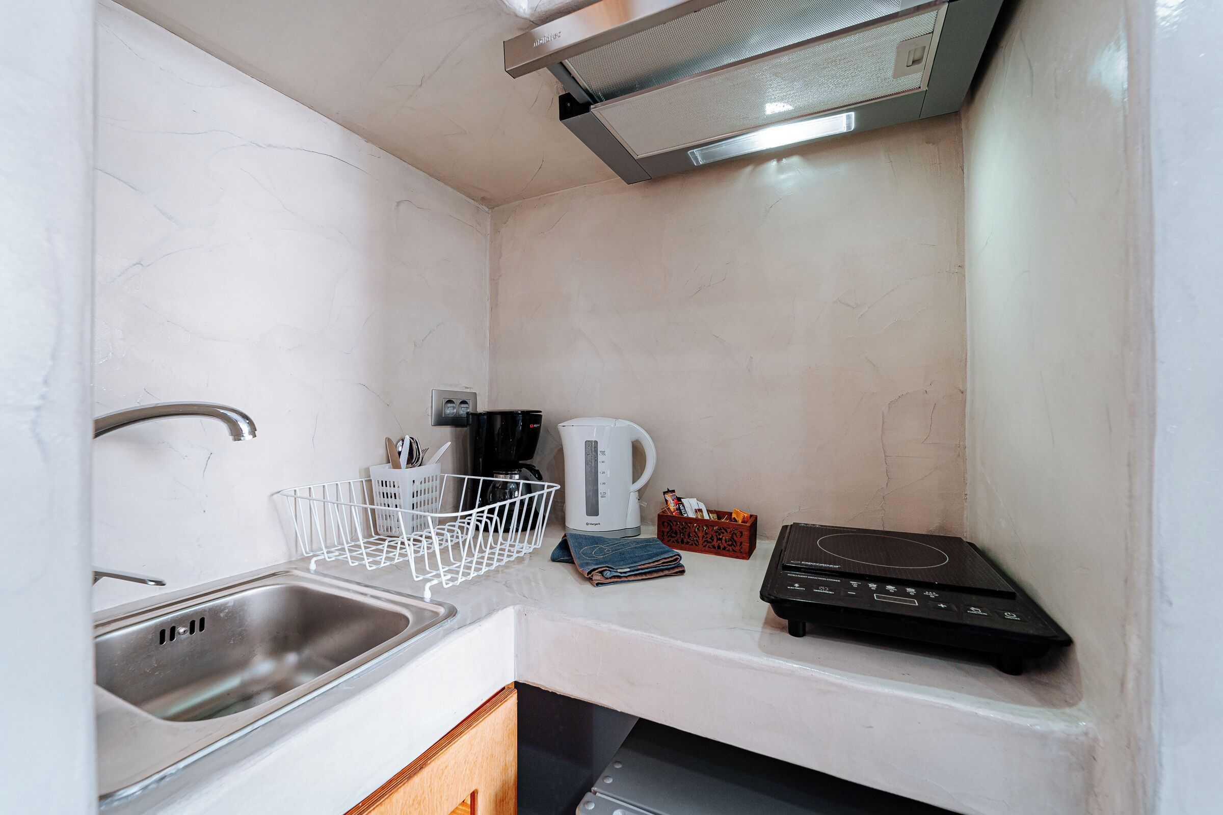 A compact kitchen with a sink, kettle, coffee maker, and induction cooktop.