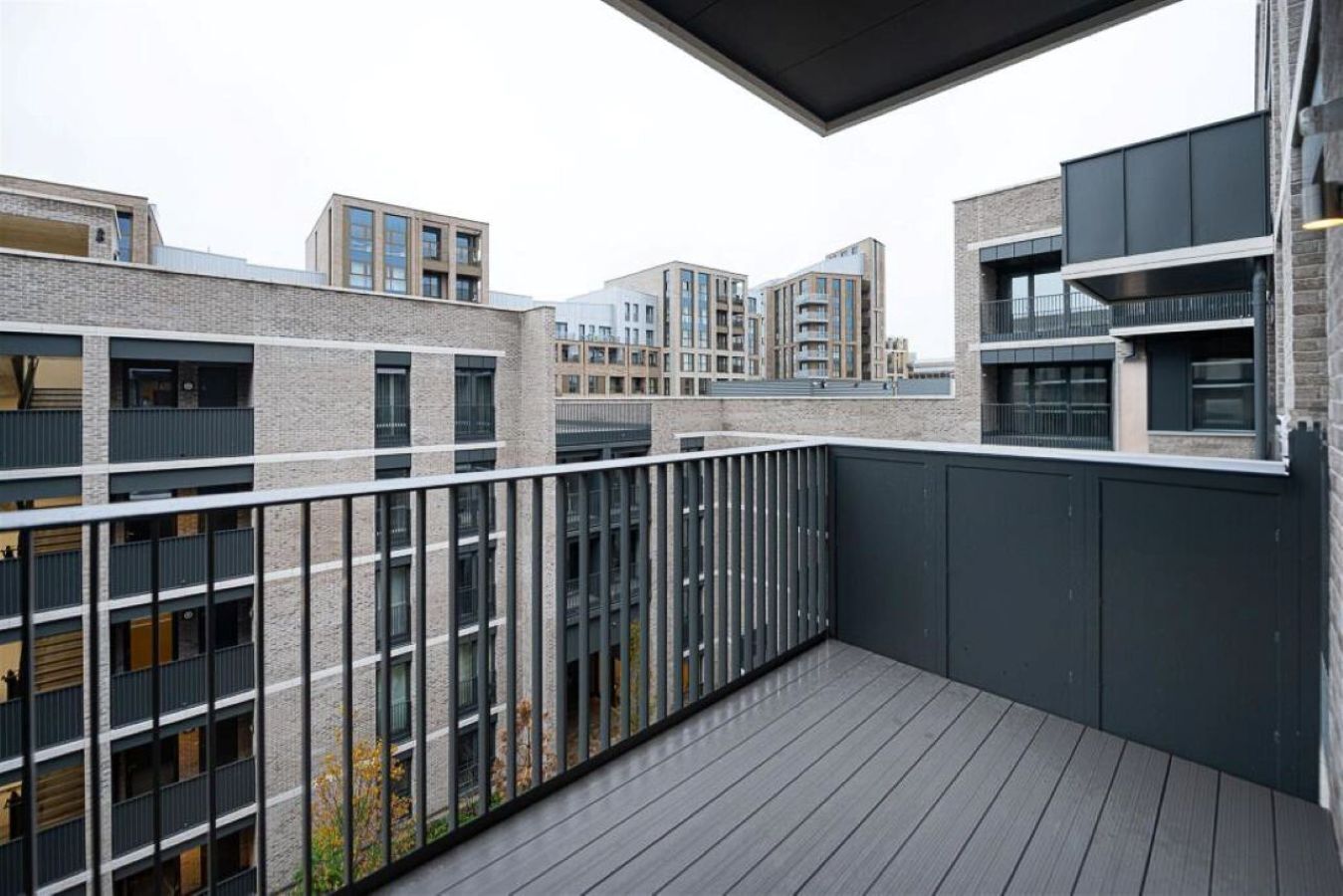 Un edificio residencial moderno con un balcón que tiene una cubierta de madera y barandas metálicas.