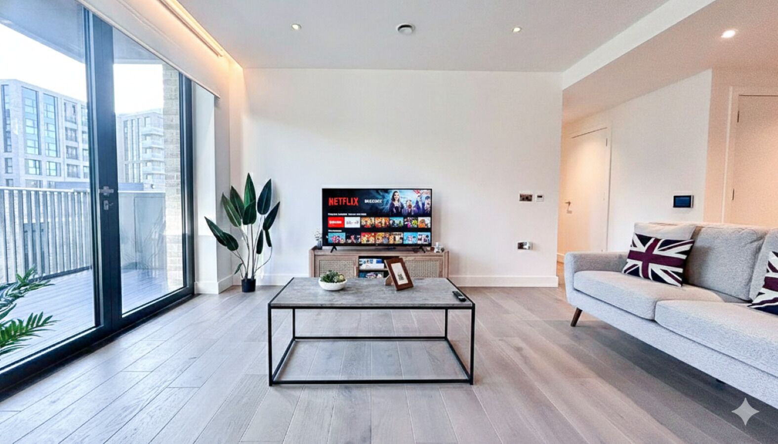 Een moderne woonkamer met een groot raam, een flatscreen televisie, een bank en een salontafel.