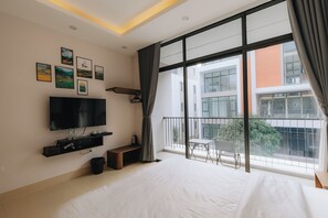 Un dormitorio moderno con una cama grande, un televisor de pantalla plana, una mesita pequeña y un balcón con vistas a la ciudad.