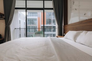 A hotel room with a large bed, a wooden headboard, and a view of a building through floor-to-ceiling windows. - Amanda Homestay - Vinhomes Ocean Park 3 (Nghia Tru)