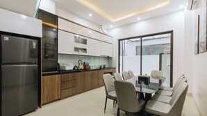 A modern kitchen with a built-in refrigerator, wooden cabinets, and a dining area with a glass table and chairs.