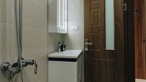 A bathroom with a shower, a sink, and a wooden door.