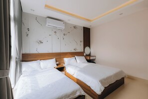 A hotel room with two beds, a wooden headboard, a wall-mounted air conditioner, and a bedside table with a mirror. - Amanda Homestay - Vinhomes Ocean Park 3 (Nghia Tru)