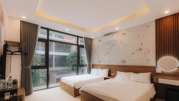 A hotel room with two beds, a large window, a wall-mounted air conditioner, and a bedside table with a mirror.