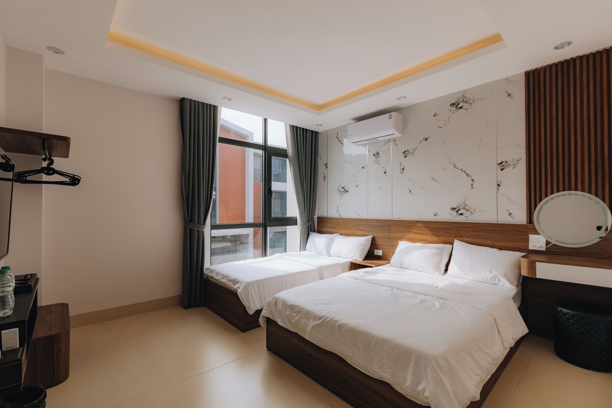 Habitación de hotel con dos camas, un armario, un escritorio, una silla, un espejo y un equipo de aire acondicionado.