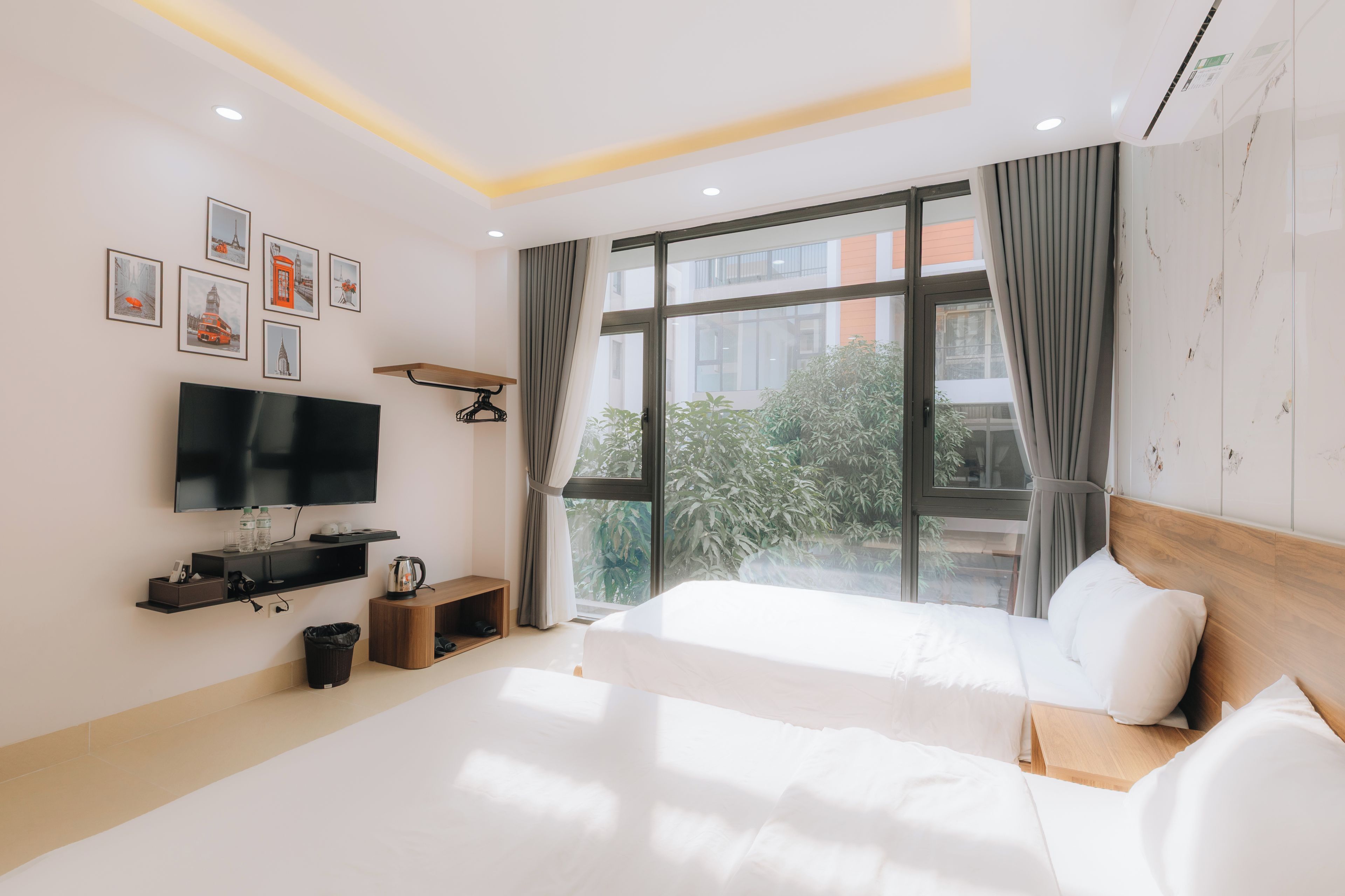 Una camera d'albergo moderna con un letto grande, una TV a schermo piatto, un comodino in legno, una piccola mensola con oggetti e una finestra con tende.