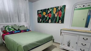 Ein Schlafzimmer mit einem Bett, einem Schminktisch, einem Gemälde und einem Fenster mit Vorhängen.