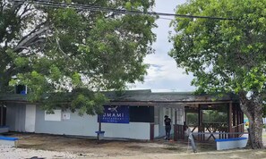 A restaurant named "UMAMI RESTAURANT" with a signboard, a person standing near the entrance, and a partially damaged building structure. - Dolphin Beach Villages / The Little Jungle (Guánica)