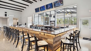 A spacious bar area with a long counter, multiple bar stools, and large windows offering a view of the outdoors. - Everstead Cottage - Cabin 3 (Plantersville)