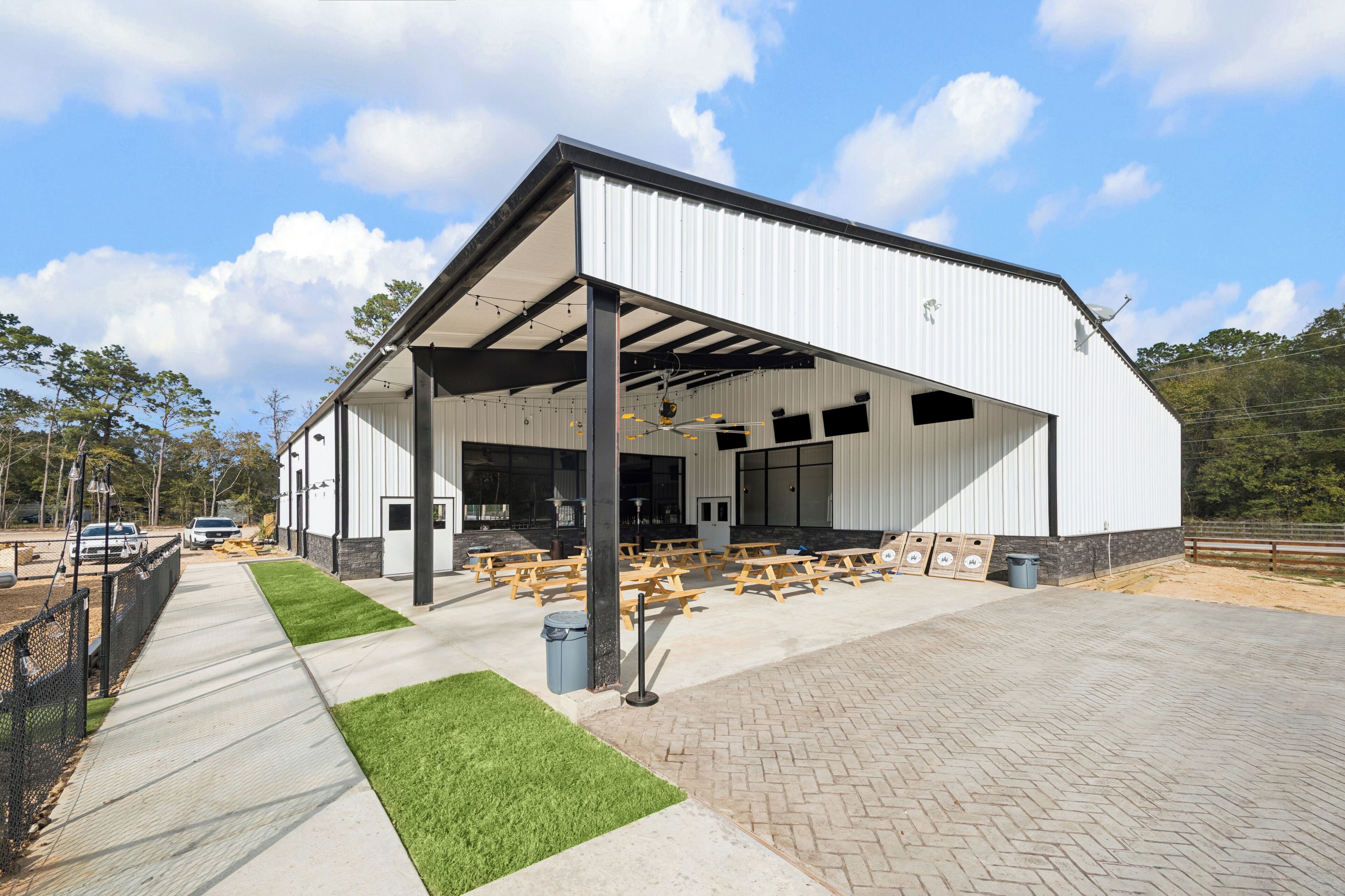 A large, modern building with a covered patio area, picnic tables, and a paved walkway.