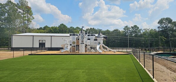 A playground with slides and climbing structures, surrounded by a fenced area and a building in the background.