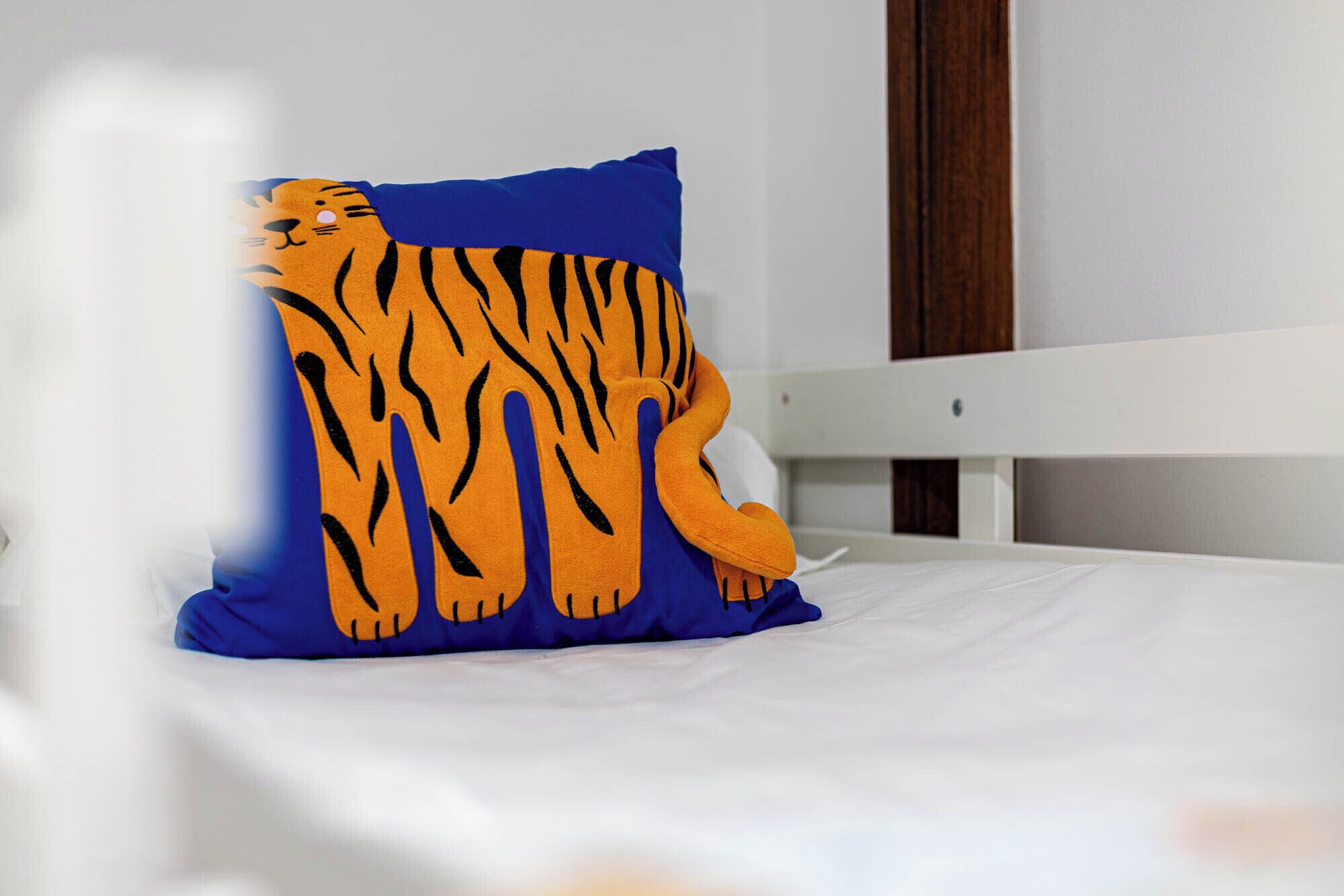 A bed with a white mattress and a blue pillow featuring a tiger design.