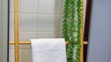 Et hvidt håndklæde hænger på en træhåndklædeholder i et badeværelse med fliserede vægge og en grøn plantepryd.