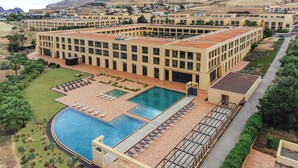 Un hotel con una amplia piscina, varias zonas de descanso y vistas a un paisaje montañoso.