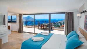 A hotel room with a large bed, a balcony with a view of the sea, and a dining area with a table and chairs. - Villa Vala in Kalkan (Kaş)