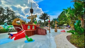 Un parque acuático con área de juegos temática de barco pirata, tobogán acuático y un sendero pavimentado.
