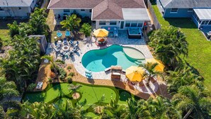 Vue aérienne d’un quartier résidentiel avec une piscine, du mobilier de jardin et des palmiers.