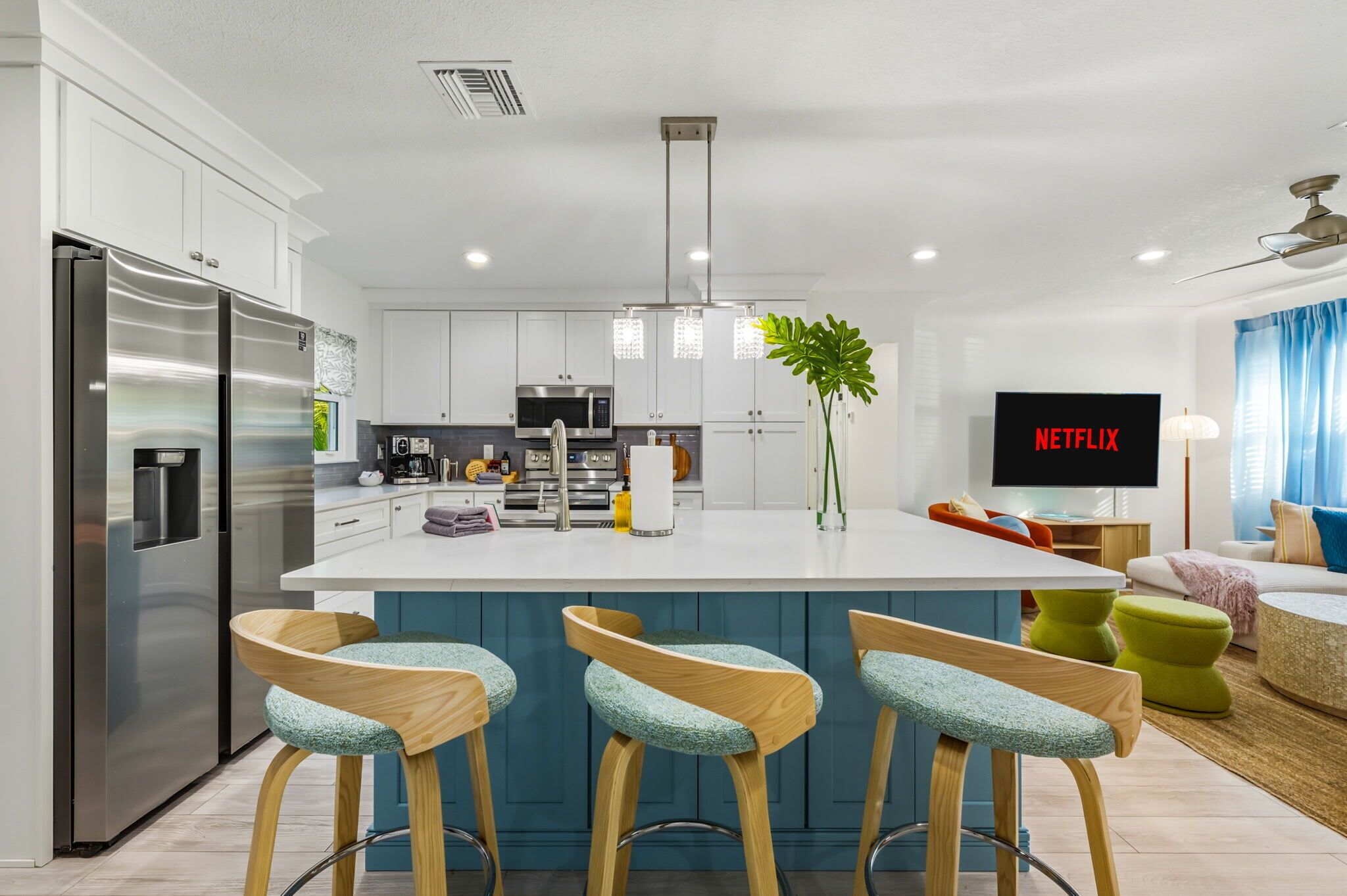 A modern kitchen with a central island, bar stools, a refrigerator, and a flat-screen TV displaying 'NETFLIX'.