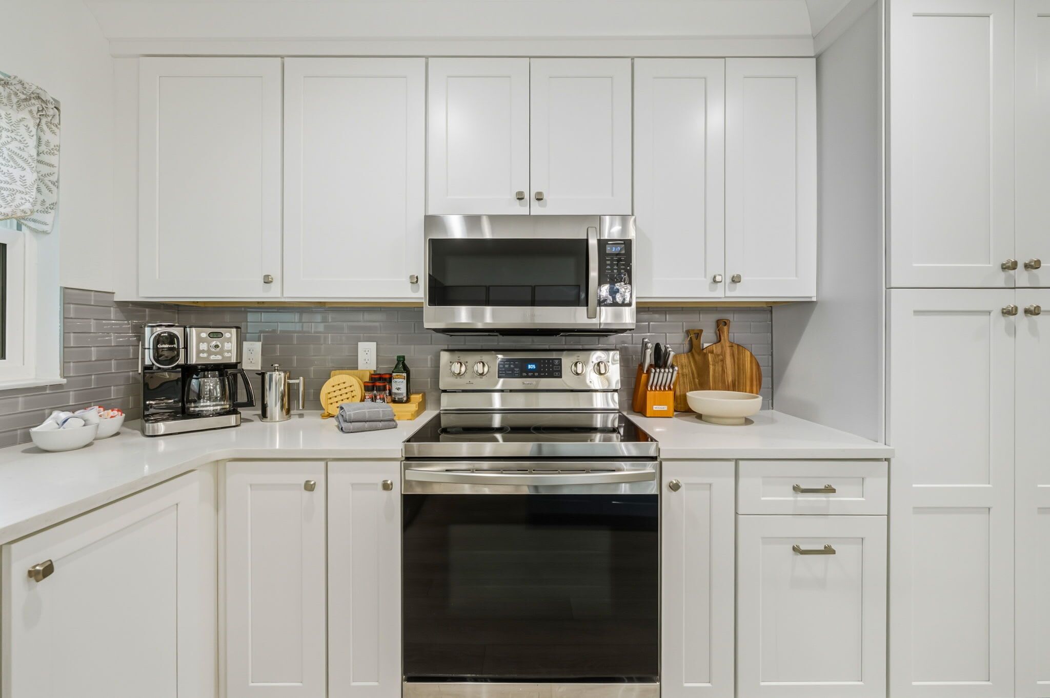 A kitchen with white cabinets, a stainless steel microwave, a coffee maker, and a toaster.