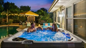 Un bain à remous avec une piscine, un patio couvert et une maison dot ée de grandes fenêtres.