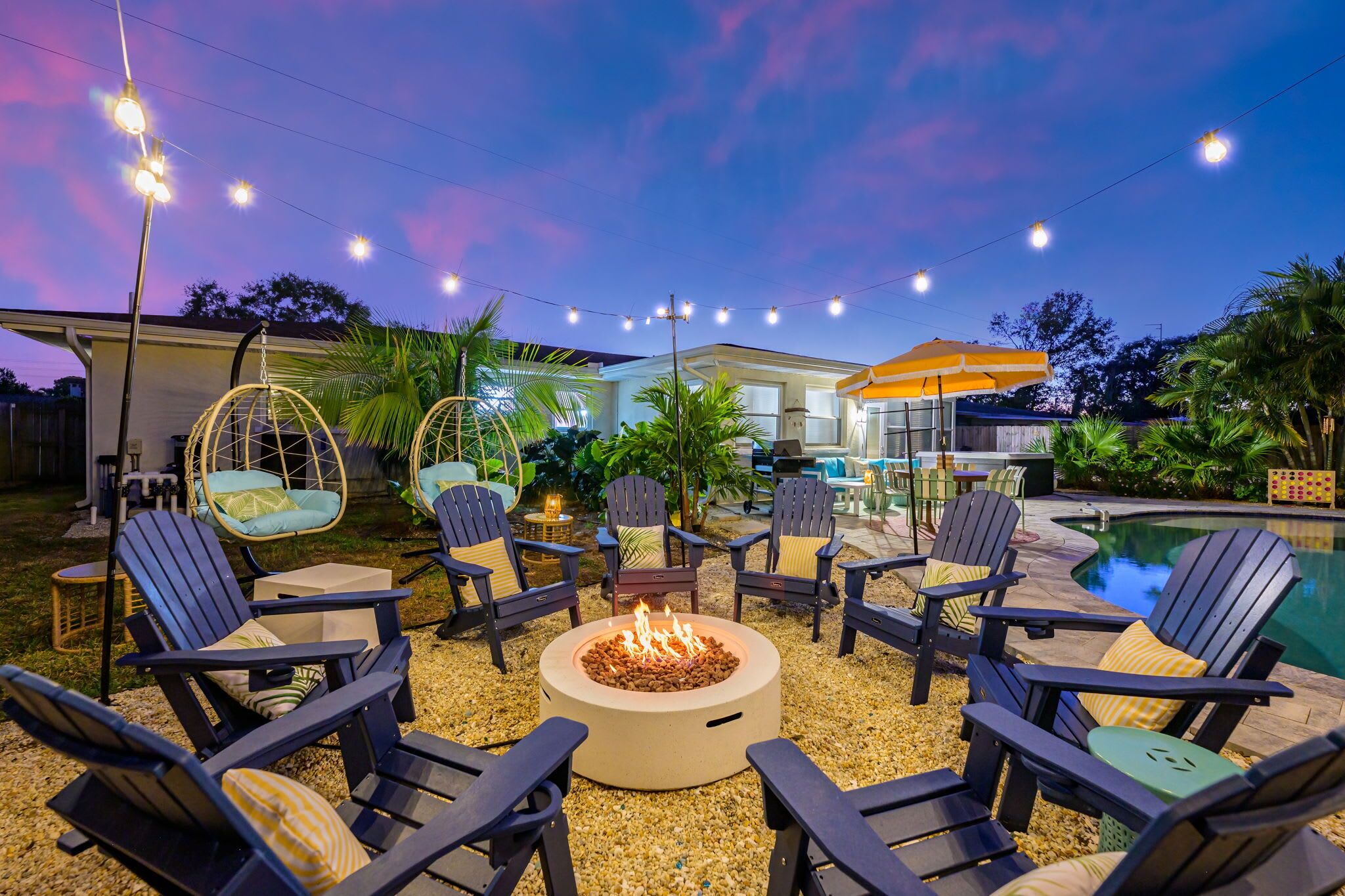 An outdoor seating area with Adirondack chairs, a fire pit, and string lights.