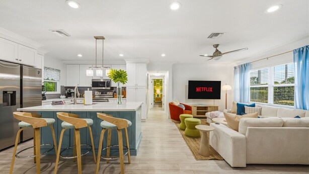 Une cuisine moderne dotée d’un îlot central, un espace de vie avec un canapé et une télévision, et un coin repas avec une chaise rouge.