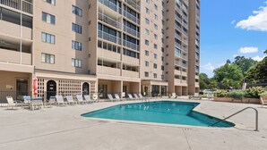 Un hotel amb piscina, gandules i un edifici alt al fons.