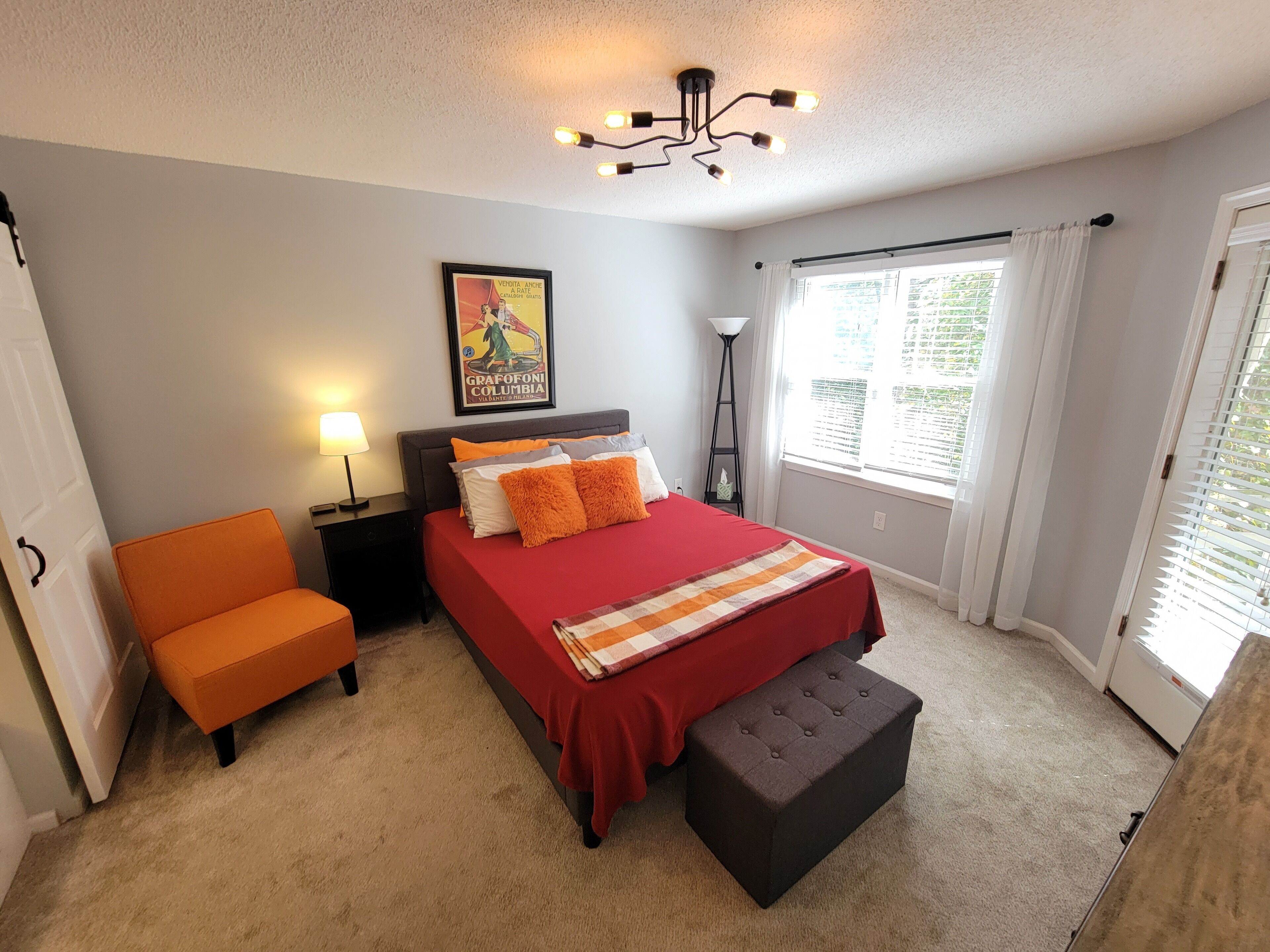 A bedroom with a bed, a chair, a nightstand, a floor lamp, and a window with curtains.