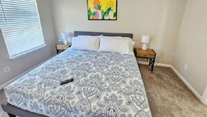 Ein Schlafzimmer mit einem Bett, zwei Nachttischen, einem Fenster mit Jalousien und einem an der Wand hängenden Bild.