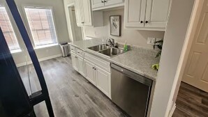 A kitchen with white cabinets, stainless steel appliances, and a window with blinds. - Hampton Oaks Hideaway (Columbia)