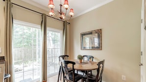 A dining area with a round table, four chairs, a chandelier, a potted plant, and a framed picture on the wall. - Classy 3 br Townhouse (Lexington County)