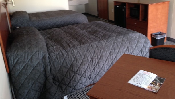 A hotel room with a bed, a desk, a chair, a television, a mirror, and a window. - Crossroads Lodge (Pender)