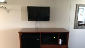 A room with a television mounted on the wall, a wooden cabinet with a microwave, and a framed picture on the wall. - Crossroads Lodge (Pender)
