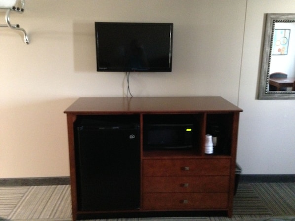 A room with a television mounted on the wall, a wooden cabinet with a microwave, and a framed picture on the wall. - Crossroads Lodge (Pender)