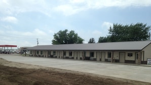 A motel with a row of single rooms, a gas station in the background, and a dirt lot in the foreground. - Crossroads Lodge (Pender)