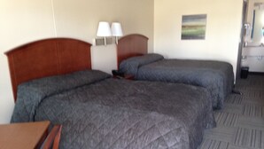 A hotel room with two beds, a desk, a chair, a lamp, and a painting on the wall. - Crossroads Lodge (Pender)